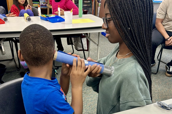 A student participating in the HPREP Junior program listens to a mentor's heart with a homemade stethoscope. 