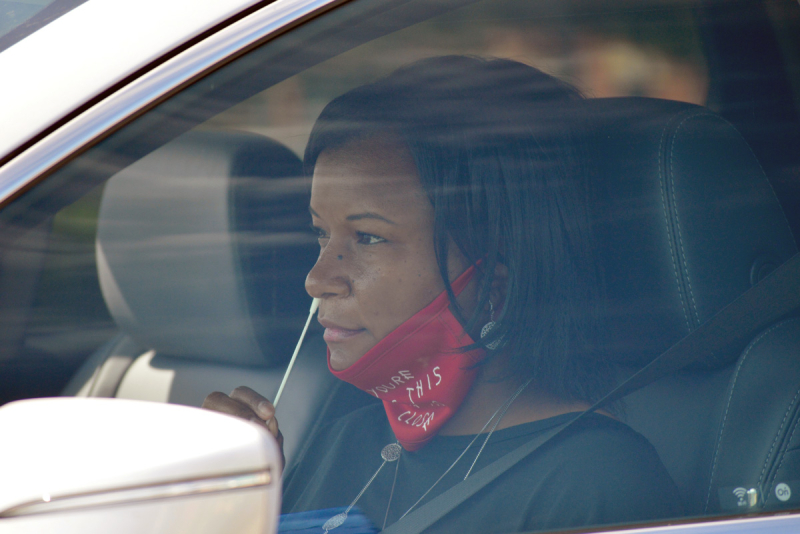 Woman giving herself a nasal swab in her car at drive-in COVID testing site.