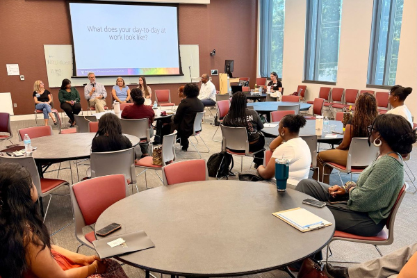 A group of people sitting around tables looking towards the front of the room where there is a group panel